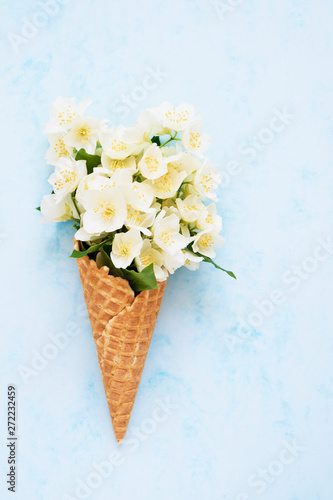 Philadelphus or mock-orange flowers in a waffle ice cream cone on blue background. Summer concept. Copy space, top view.