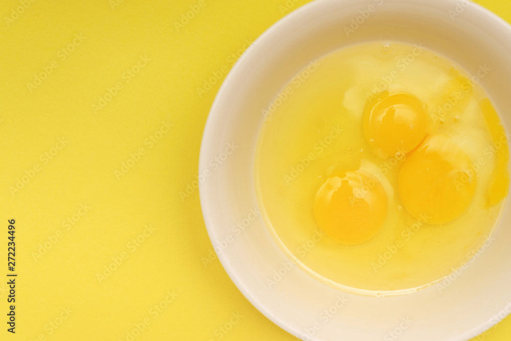 three broken chicken eggs in a plate. fresh raw protein food. yellow background. three broken chicken eggs in a plate. fresh raw protein food. yellow background.