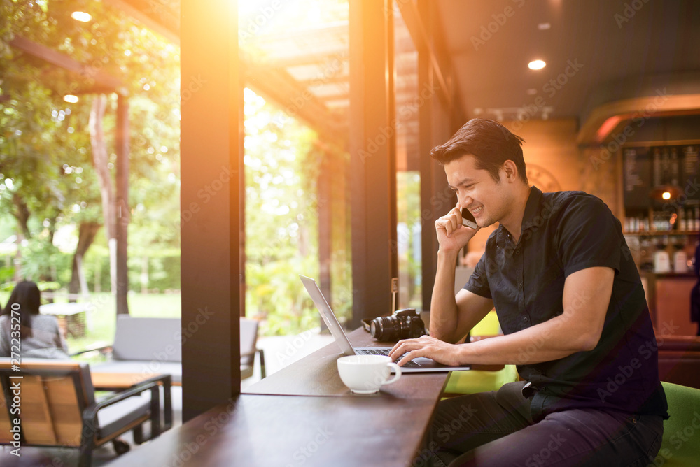 Stylish modern guy talking with a smartphone and using a laptop in a coffee shop Stylish modern guy talking with a smartphone and using a laptop in a coffee shop