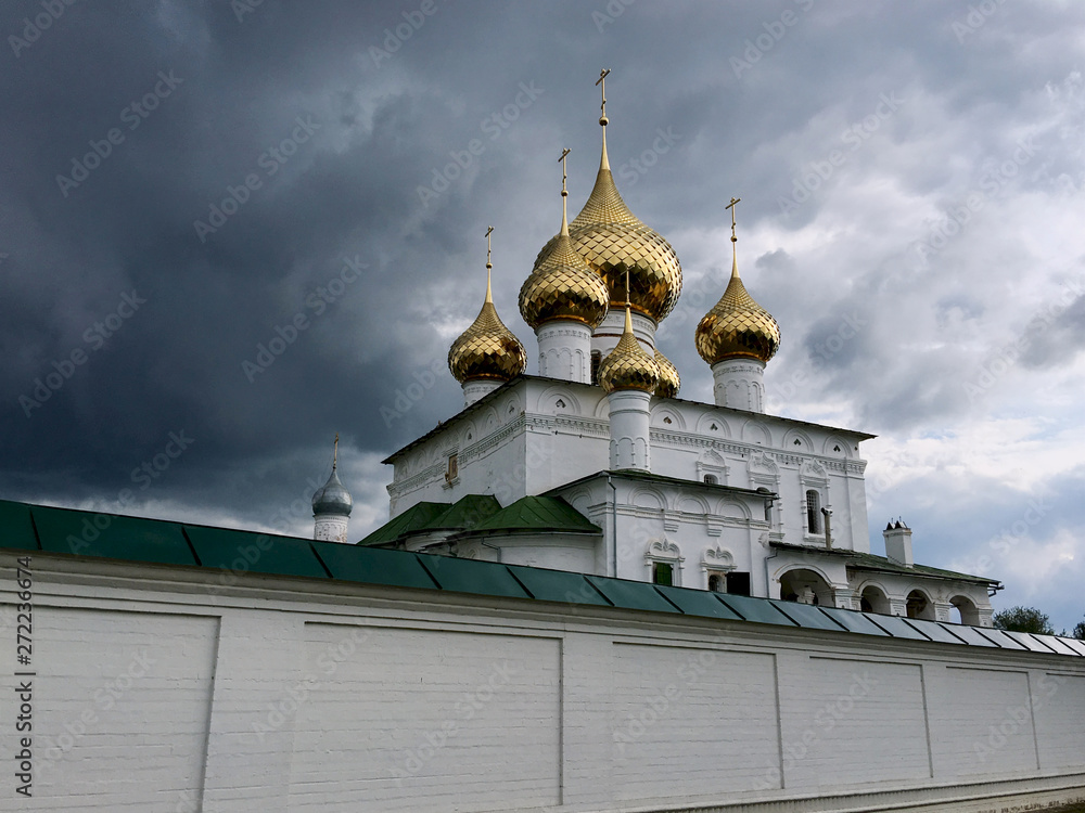 Golden domes of the Orthodox church and the white temple walls against the background of a stormy gray sky, Resurrection Monastery 15th century, Uglich City, Russia