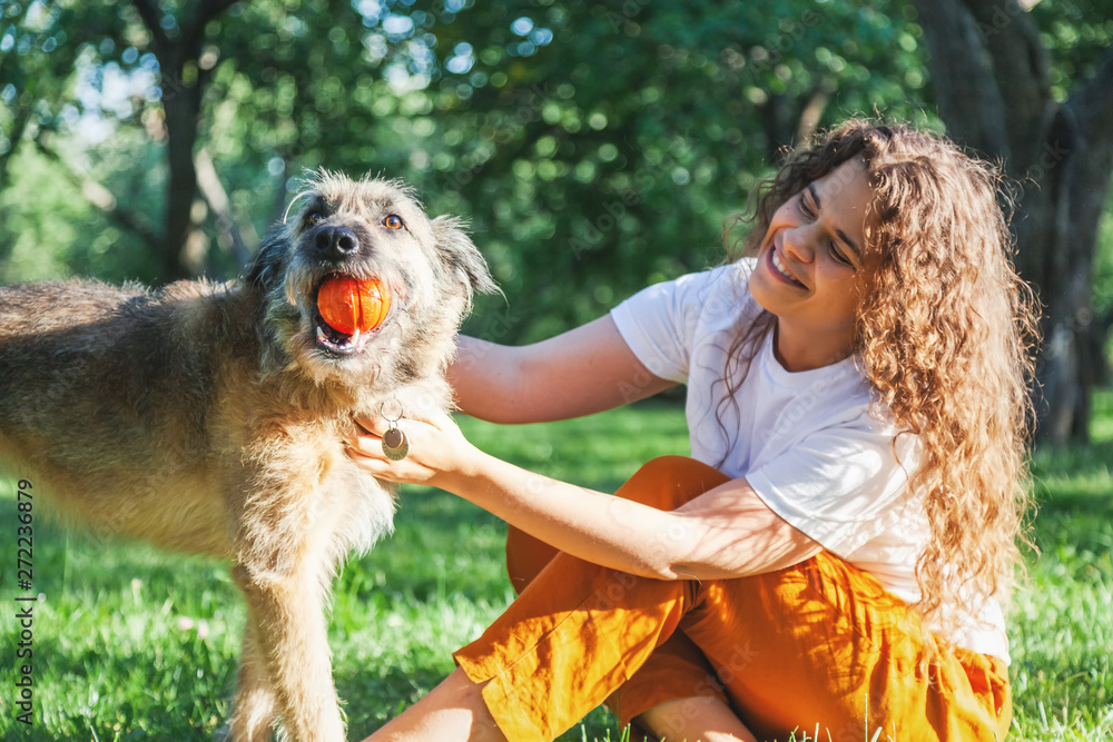 Young happy charming girl playing with her dog with a ball in the park