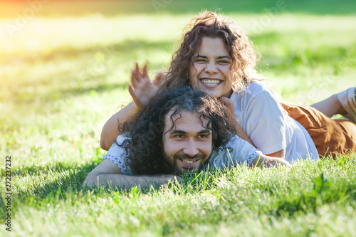 Happy young curly couple lying on the green grass in the summer sunny park