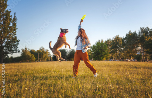 Fotografie, Obraz Young beautiful curly girl playing with her dog with a  frisbee in summer park