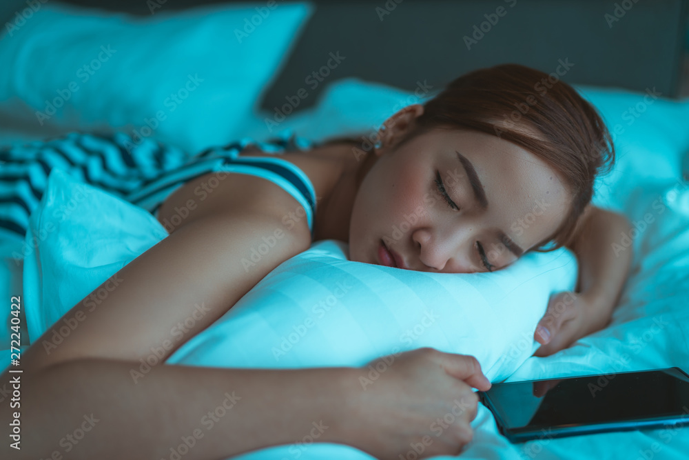 Close up portrait of a woman tired and sleeping in an hotel bed with a mobile phone Close up portrait of a woman tired and sleeping in an hotel bed with a mobile phone