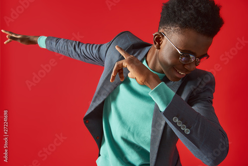 Cheerful Afro American man in glasses dancing on red background