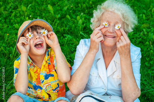 Happy grandmother and grandchild fooling around the lawn of putting chamomiles instead of eyes. Family love and relationships. Family happy holiday.