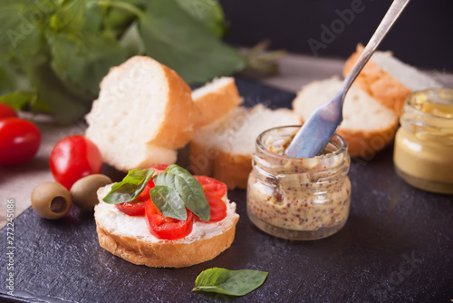 Italian bruschetta with cream cheese, tomato cherry and bazil and cutting bread on the plate with small bottle of mustard