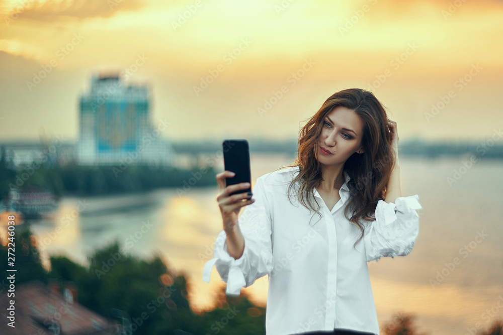 Woman making self portrait with her smart phone over cityscape golden sunset Woman making self portrait with her smart phone over cityscape golden sunset
