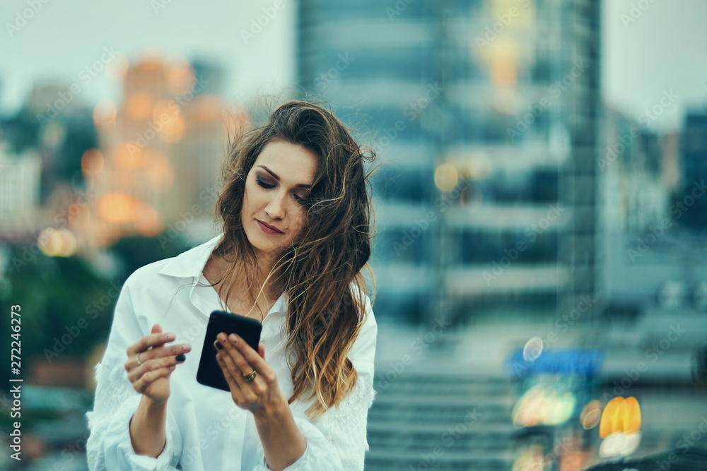 Fototapeta premium Young woman over cityscape holding a smart phone texting