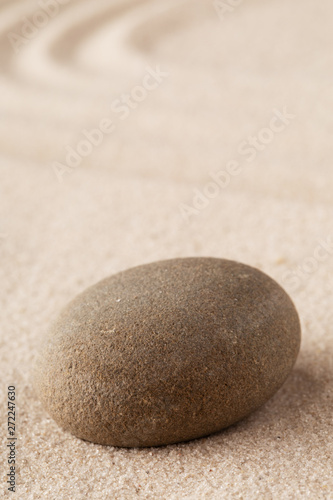 Zen garden meditation stone. Round rock on sandy texture background.
