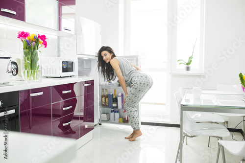Young woman on the kitchen opening a fridge. Female indoors in the morning. Cheat meal. glutton girl.