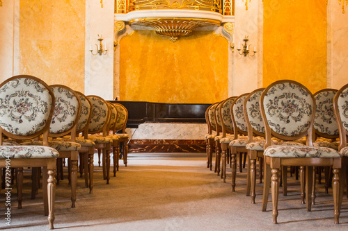 a group of vintage wooden chairs stands in several rows in a large old room with a luxurious interior. empty auditorium in the assembly hall. hall for performances without spectators photo