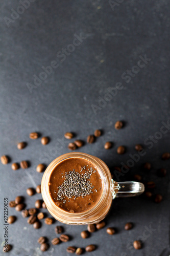 Organic natural chocolate coffee cacao smoothie beverage with chia seeds in glass jar on a black graphite slate background with coffee beans  top view. Healthy diet vegetarian snack. Free copy space