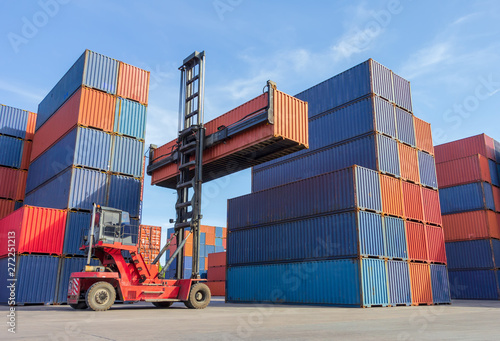Forklift handling container box loading to truck in shipping yard with cargo container background.