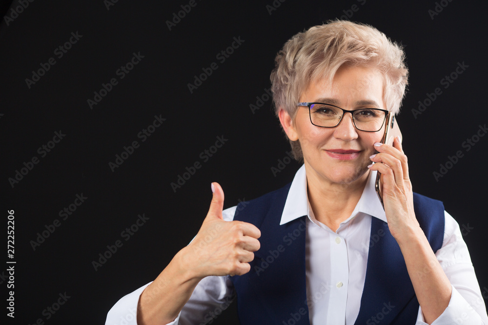 beautiful stylish aged woman in glasses in waistcoat on a black background calls on the phone beautiful stylish aged woman in glasses in waistcoat on a black background calls on the phone