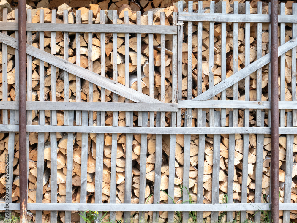 Firewood stacked in a woodpile behind the fence in the open air.