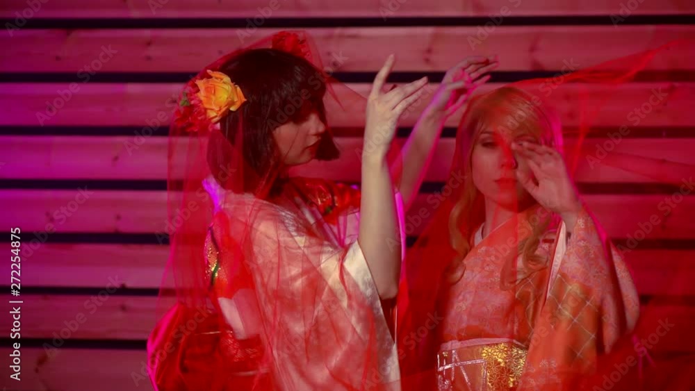 Portrait of two geisha girls on a pink background, they throw on a transparent red tulle. Portrait of two geisha girls on a pink background, they throw on a transparent red tulle.