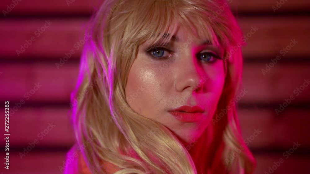 A close-up portrait of a blue-eyed blonde girl with bangs, she is in a Studio with pink lighting, her hair fluttering in the wind. A close-up portrait of a blue-eyed blonde girl with bangs, she is in a Studio with pink lighting, her hair fluttering in the wind.