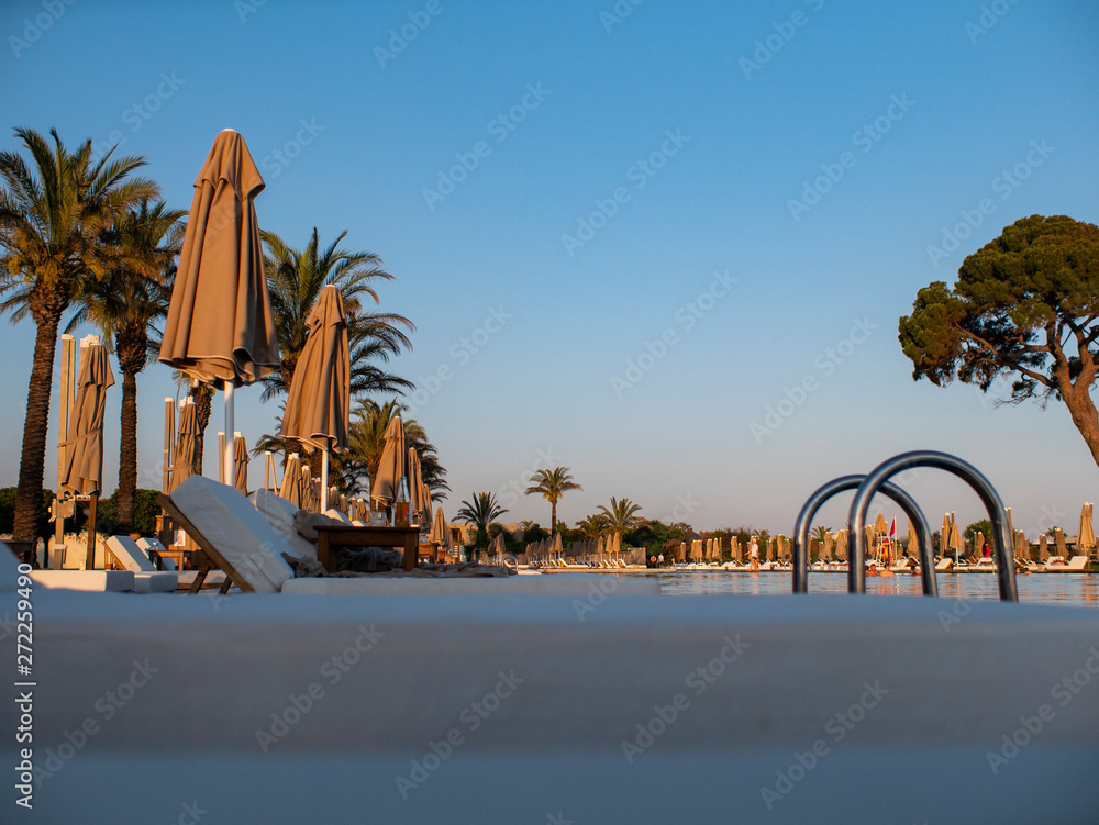 Fototapeta premium sunbeds and umbrellas near resort's pool . Sun beds and umbrellas at the poolside