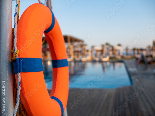 Orange lifebuoy near public swimming pool On a blurred background, a swimming pool is visible
