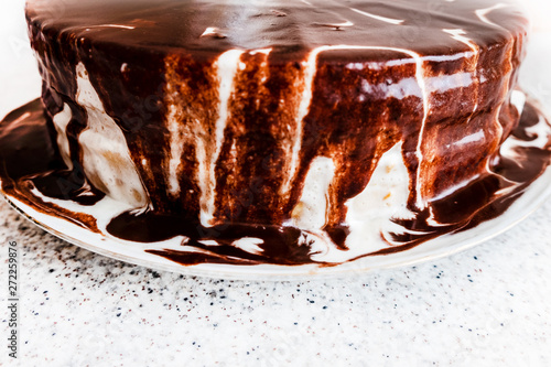Appetizing homemade cake, poured with black and white cream of sour cream and chocolate flowing along the edges