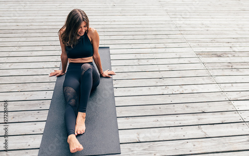 Smiling woman resting after yoga training outdoors, sitting on a mat
