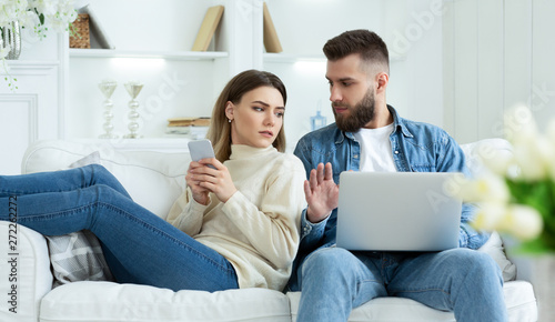 Woman Spying Husband's Laptop, Sitting Together On Sofa