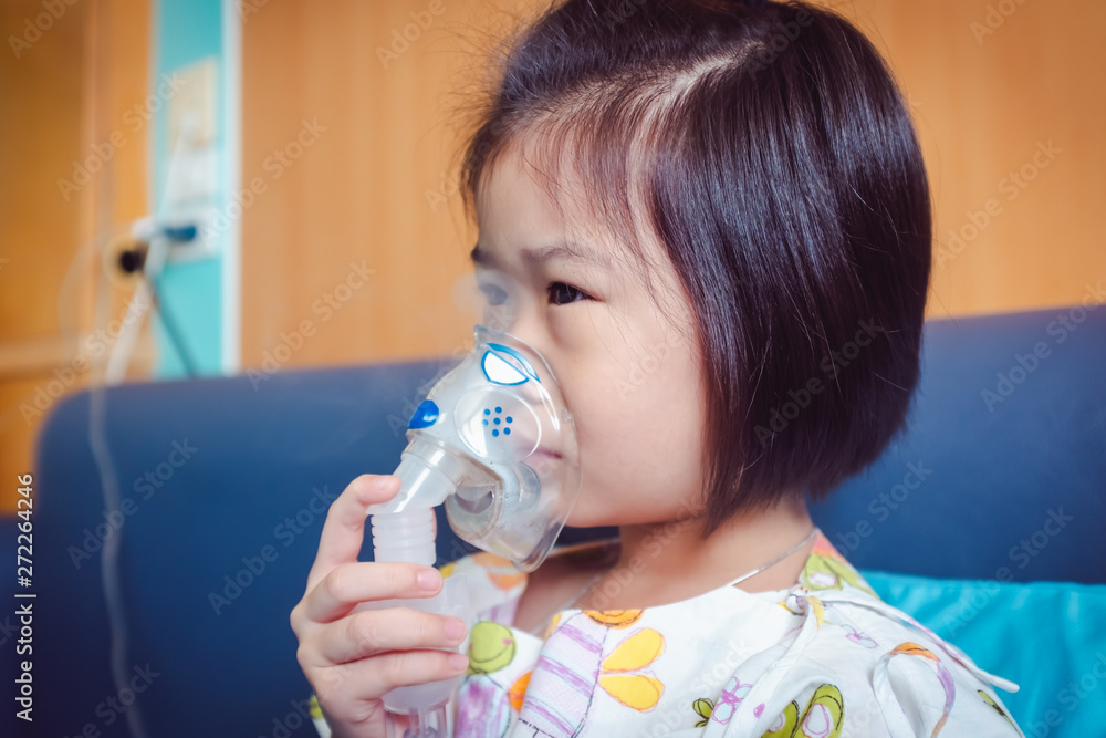 Sad asian child holds a mask vapor inhaler for treatment of asthma. Breathing through a steam nebulizer.Illness girl admitted in hospital.