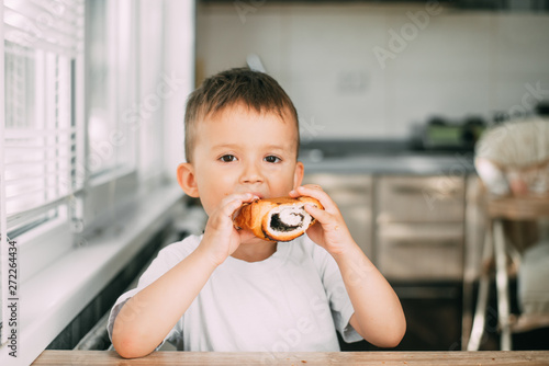 charming child in the kitchen during the day eating a bun with poppy seeds  very tasty