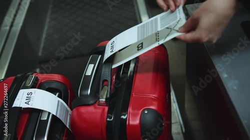 Close-up of female hands placing baggage-claim ticket around red suitcase handle. Airport terminal. Cinematic shot on RED camera.