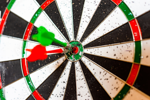 A round board for playing darts close up, red and green darts hit the target.