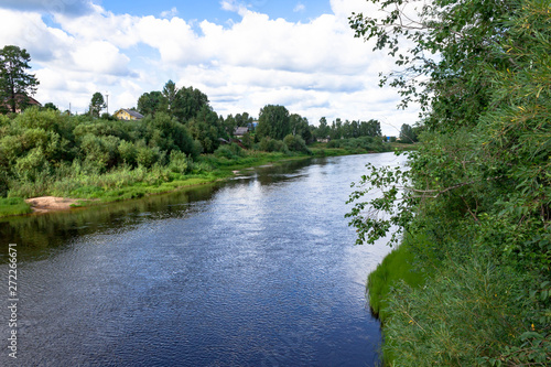 Summer river village landscape. Sandy beach on bank  green grass and trees blue river and cloudy sky