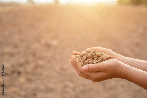 Young farmer holding dry soil in empty land for planting