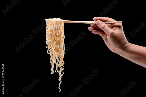 Fotografie Hand holding bamboo chopsticks and fork over instant noodles
