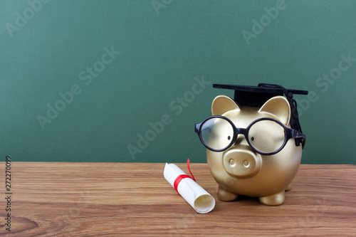 Fotografie Gfold piggy bank with a grad cap and diploma in front of green chalkboard
