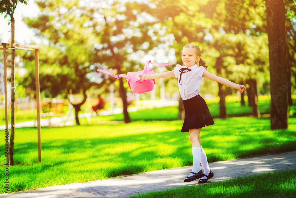 Portrait of happy Caucasian young smiling girl wearing school backpack outside the primary school. schoolgirl, elementary school student runs jumping from school, graduation, summer holidays.