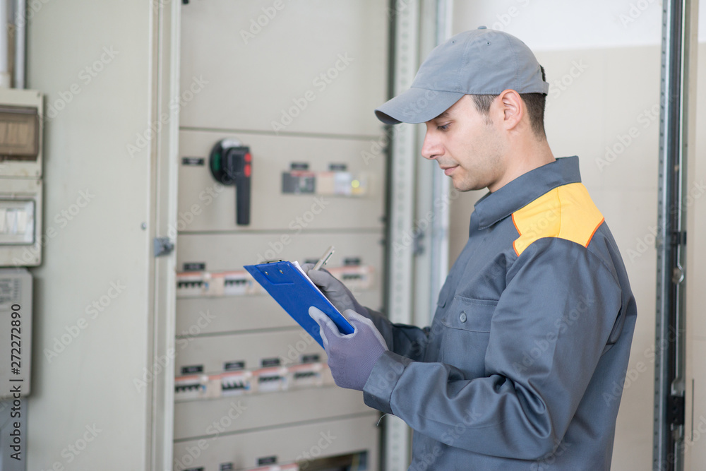 Electrician writing a document while inspecting a panel Electrician writing a document while inspecting a panel