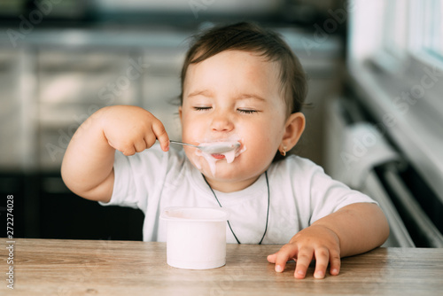 A little charming girl eats yogurt all smeared herself