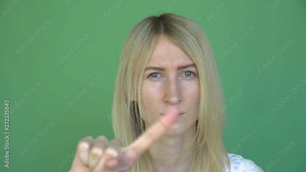 a young blond woman shakes her finger and frowns, punishes. green background. threatens a young blond woman shakes her finger and frowns, punishes. green background. threatens
