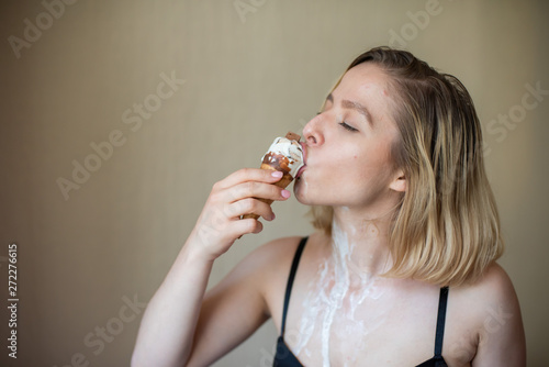 Sexy blonde licks a waffle cone. Ice cream is melting, erotically draining through the body of an attractive woman. Beautiful girl smeared with ice cream.