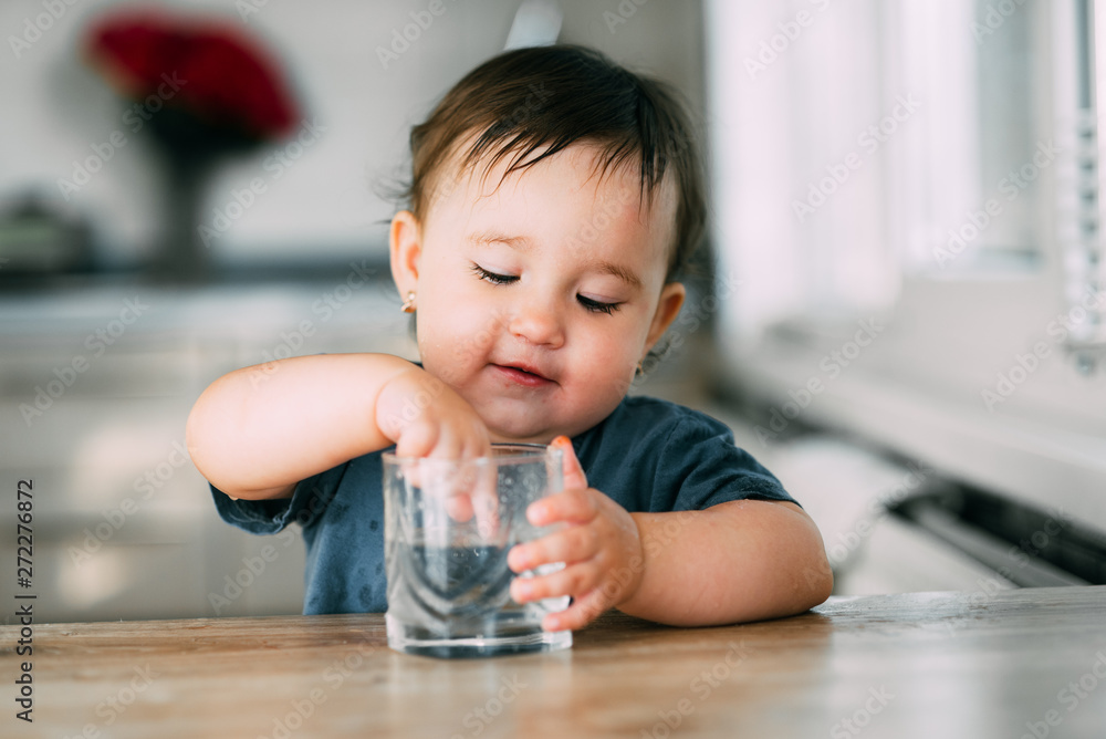 Cute little girl sitting in baby chair and drinking water