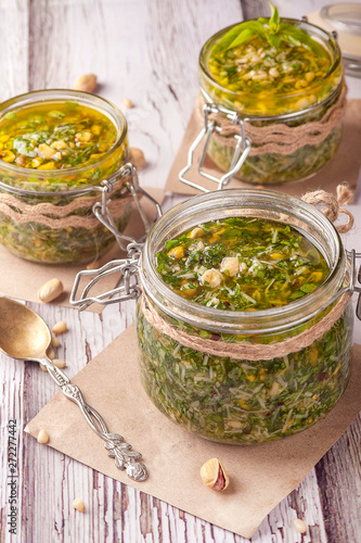 Green pesto sauce. Classic Italian sauce. Preservation in a glass jar. Three jars of sauce decorated in a rustic style.  Close up and vertical orientation.