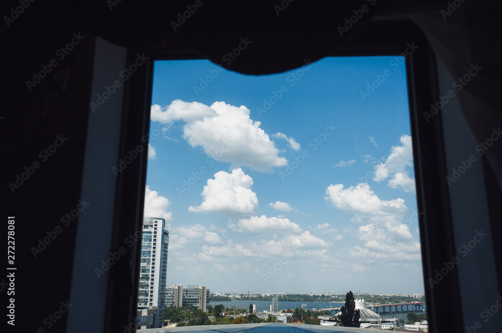 View from the window of a beautiful blue sky with clouds, on the background of a modern city with a river, a bridge.