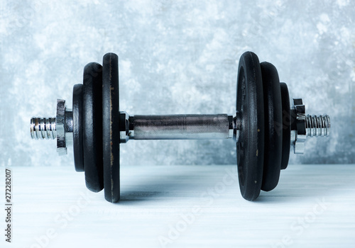 Black heavy dumbbell on rustic wooden background. Fitness or bodybuilding background Copy space. 