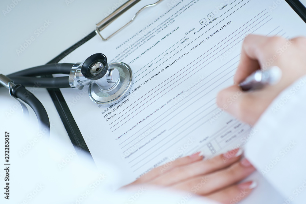 View from behind of female medicine doctor hand holding silver pen writing something on clipboard close-up. Ward round, patient visit check, medical calculation and statistics concept. View from behind of female medicine doctor hand holding silver pen writing something on clipboard close-up. Ward round, patient visit check, medical calculation and statistics concept.