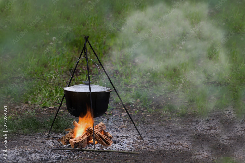 Outdoor country side cuisine with cauldron metal pot kettle for cooking outdoor in the middle of the nature near the camp with the campfire, cooking at the camp fire traditional dish. Space for text Outdoor country side cuisine with cauldron metal pot kettle for cooking outdoor in the middle of the nature near the camp with the campfire, cooking at the camp fire traditional dish. Space for text
