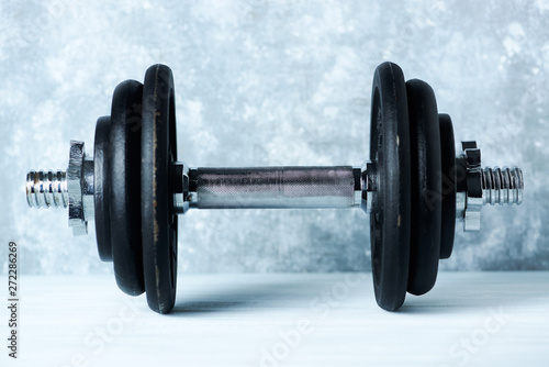 Black heavy dumbbell on rustic wooden background. Fitness or bodybuilding background Copy space. 