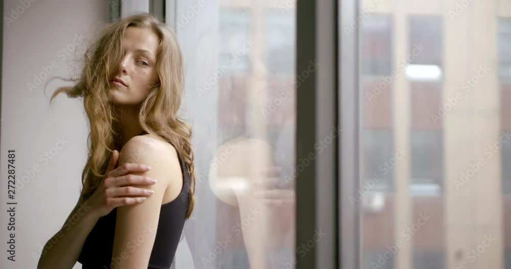 Portrait of a slender model posing on the windowsill of a large panoramic window. Her hair is blowing in the wind. Portrait of a slender model posing on the windowsill of a large panoramic window. Her hair is blowing in the wind.