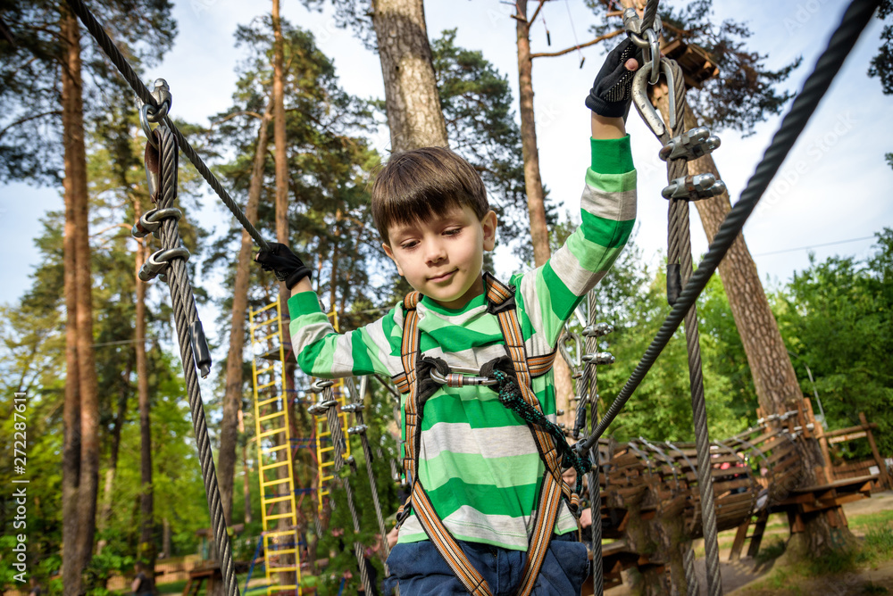 boy climbs in a high wire park above the ground. ziplining. boy on the zip line. kid passes the rope obstacle course