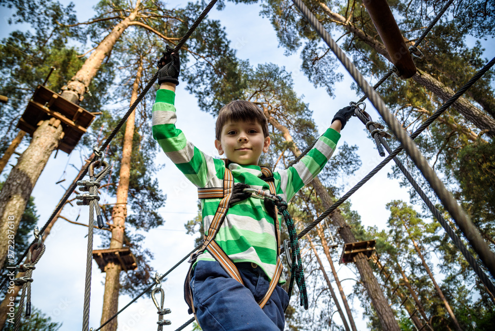 boy climbs in a high wire park above the ground. ziplining. boy on the zip line. kid passes the rope obstacle course boy climbs in a high wire park above the ground. ziplining. boy on the zip line. kid passes the rope obstacle course